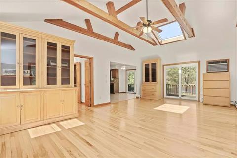 Family room with a vaulted ceiling with custom beams, ceiling fan and skylights.