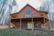 HILLTOP HEAVEN! Magnificent Log Chalet sits in its own mini forest approximately 5 minutes from Uptown Kingston. This 2 bedroom, 2 bath, 1180 square foot home has open beamed cathedral ceilings, imposing beams and open stairways with look down landings, wrap around porch/balcony, and attached spacious drive through carport. Imagine walking out of the spacious living room to relax on the front balcony or looking out the upstairs bedrooms with views of the sunsets over the the Catskills. Deer, birds and woodland creatures abide in your woods. Your friends, family and pets will love you for bringing them here. With 2.5 acres there is dream potential for subdivision or a cottage/guest home, gazebo, patio/fire pit, swimming pool, gardens, pond, nature trails. Equipped with a Navien high efficiency system with propane as its source, new septic, central air ability, community water, and underground electric. Designer Wolf Classic kitchen cabinet package waiting for your installation. Sheetrock on site to be installed and prepaid blown insulation. All included as part of the price!