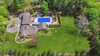 Tucked away on a fully fenced, over two-acre, park-like, electronic-gated property, stands a sprawling Farm Rach expanded and remodeled in 2007. This 5, 400-square-foot mini estate of your dreams is located in the scenic Upper Brookville village. With rolling wooded open spaces rife with wildlife and dotted with grand and historic estates, you will be close to boating, golf, equestrian facilities, quaint village shopping, museums, and Long Island Railroad with about a 40-minute commute to Manhattan. Within about a mile radius of your home you will find four golf courses, a produce farm, a nursery (both with stores), and mansion museums and preserves. Oyster Bay, Locust Valley, and East Norwich villages are just a little farther away.Surrounded by sprawling, level lawns bounded by rows of evergreens and split-rail fences, the main building wraps around a delightful outdoor entertainment complex with large Gunite, saltwater pool, with hot tub and water feature, expansive bluestone patios, and a large, covered cooking pavilion with ample bar seating. Think of the fabulous summer parties you can enjoy in this inviting setting. At the end of the pool, a garden offers colorful plantings, fruit frees and a privacy wall of evergreens. On the east side of the pool, a free-standing, legal guest cottage may invite its guest to an early morning dip, and on the west side, a large recreation room, with full bath, walk-in closet, a large pub-like wet bar with wine cooler, a game area, and a home theater, can serve as a great cabana party room.A bookcase-lined hall leads from the pool party room into the sitting room of a large in-law suite that includes a summer kitchen, laundry room, luxury full bath, and bedroom. A hall opens from the apartment into the main house where a banquet-sized dining room creates a Tuscan atmosphere with a stone fireplace and open-beam ceiling. The spacious eat-in kitchen has similar open-beam ceiling and rustic lighting. It offers extensive cherry cabinetry, granite counters, several windows overlooking the front courtyard, a huge center island with wine cooler, a walk-in pantry, and high-end stainless-steel appliances, including a double wall oven with convection, and a six-burner glass cooktop beneath a custom copper exhaust hood. The spacious, sunny, two-story entrance foyer, with powder room, features a staircase, with ornate iron balustrade, ascending to a second-floor balcony. The adjoining, spacious and welcoming living room provides sunny views through huge front and rear windows, a closet, and access to the attached two-car garage. Two steps down from the foyer and kitchen, an immense, sun-drenched four-season room features stone floors, huge windows overlooking the pool and patio, access area the pool, and a stone corner wall housing an arched wood-burning oven/fireplace; perfect for pizza parties.On the second floor, a balcony with study area leads down a hall to two bedrooms, a hall bath, and the primary bedroom wing. This private retreat offers a spacious bedroom with ample windows, two walk-in closets, and a luxury marble bath with walk-in shower, twin vanities, and whirlpool tub. Accessed from the entrance foyer, the partial basement has a spacious gym area, a laundry area, and room for ample storage. Additional features include: central vacuum; two fireplaces; electronic gate; smart thermostat; fully-fenced property, second fence around pool area; whole-house entertainment system with speakers; Energy Star appliances; hardwood floors where seen; and fruit trees (apple, pear, peach). Offering so many possibilities for the various areas of this expansive home and on such a beautiful level property, with sweeping lawns and shady tree areas, this amazing mini-estate is ready for you to move in and start living the life your dreams. View 3D tour & floor plan.