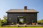 A notable jewelry designer and artist designed and infused her homestead on 13.5 acres in Germantown with the spirit of her upbringing among the Maasai in Africa. The two houses on the property embody an aesthetic that merges both utter simplicity with the luxury of texture and color. The pair of barns-turned-homes bracket the end of the driveway. Each is wrapped by porches and has soaring windows and vast doors that open to nature and invite light and views. Imagine gathering at dusk under the fragrant canopy of the sprawling catalpa tree or finding communion with the earth on an early morning walk. Exposed beams, natural wood trestle tables, stone countertops, lofts, and open floor plans create the illusion that inside and outside are one and the same. Sinks and other fixtures forged of unadulterated metal and walls of rough-hewn wooden blocks are examples of a space curated by a sensibility both elemental and artful. The main house has four fireplaces that share an enormous brick chimney that rises proudly through the center of the building. There is a clawfoot or pedestal tub on every floor, including one outside, forged of hammered copper. The large open floor plan that encompasses living, cooking, and dining space dominates the main floor. There is also a separate dining room, three sleeping spaces, numerous cozy nooks, and a tidy office. The second barn serves as a place for gatherings, celebration, and houseguest overflow. Interior communal spaces flow onto the outdoor spaces, including a wide porch in two sections, one covered. A tomato red clawfoot tub and picnic table pop on the roofless porch against the rich gray of the exterior walls. When there need to be doors to close, there are, but absent necessity, the theme of these houses is fluidity. Uninterrupted harmony between home and nature and among the various and often unconventionally-defined interior spaces. Walking trails through the woods and easy proximity to Hudson, Tivoli, Rhinebeck, and many Hudson Valley amenities make this property both a fantastical escape and a doorway to more.