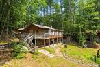 Tucked among the pines with deeded lake rights to Lake Luzerne, this 4BR/2BA rustic yet spacious camp is perfect year-round or as a vacation retreat. Features include wood-beamed ceilings, a cozy wood stove, and an open kitchen/dining/living area ideal for entertaining. Two expansive three-season rooms open to an oversized wraparound deck. Enjoy a game room with pool table, workshop, laundry, and ample storage. Set on a peaceful lot with a classic Adirondack feel, close to the lake, hiking, and Adirondack attractions.