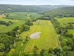 Modern Minimalist Masterpiece on 19 Bucolic Acres in Dutchess County. Welcome to a rare offering in the heart of the Hudson Valley, where striking modern architecture meets timeless pastoral beauty. Completed in late 2024, this extraordinary estate sits on over 19 acres of flat, fenced farmland at the picturesque intersection of Bethel Cross and Carpenter Hill Road. Perfectly sited on a south-facing rise along the Shekomeko Creek, this newly constructed home is a serene, sophisticated sanctuary just two hours from New York City. A bold fusion of modern, industrial, and eclectic design, the residence offers over 4, 700 square feet of light-filled, open-concept living on one level, including 3, 057+/- sq ft main house, a stunning 1, 046+/- sq ft attached greenhouse-conservatory that brings year-round indoor-outdoor living to life and a 1, 423 sq ft +/- heated garage/studio/guest apartment. Every detail was curated with intention; from yaki sugi siding and a metal Kemper roof to polished concrete floors and walls of glass that frame unspoiled views of nature. The heart of the home features a bespoke chef&rsquo;s kitchen with live-edge shelving, custom cabinetry milled from trees on the property, concrete countertops, a butler&rsquo;s pantry, and a beverage bar. Double primary suites offer en suite wood burning stoves, spa-like baths with cast iron tubs, Italian tile, and handcrafted metal vanities. Both are complimented by airy bathrooms with natural light and industrial fixtures.A gas fireplace in the ample living room, vaulted ceilings, clerestory windows, and art lighting throughout create a harmonious blend of warmth and style. This is a home designed not just to live in, but to live fully. Outside, the entire 19-acre estate is bordered by classic white 4-board oak fencing, ensuring both privacy and visual continuity. A one-acre, 10-foot-deep pond and expansive flat pastures make this a dream property for equestrians, polo enthusiasts, hobby farmers, or anyone seeking a deep connection with the land. Zoned as a horse farm within an agricultural district, it offers rare potential for animal lovers and breeders alike.Car collectors and creatives will appreciate the oversized, fully heated garage and studio space outfitted with track lighting, storage, and the flexibility to serve as an art gallery, workshop, or one-bedroom apartment. With a 3, 000 sq ft unfinished basement, covered porches, multiple patios, and estate management partners already in place, the property is as functional as it is inspiring. Additional features include an Endless Pools heated performance pool in greenhouse. The home has a sustainable, passive solar design and was constructed to allow for a future living roof/rooftop deck. New well, septic, and underground utilities. Energy-efficient systems throughout. Surrounded by horse farms and wildlife. Just minutes from the town center and Mashomack Polo Club.Whether you&rsquo;re an artist, gardener, equestrian, or collector, this unique Hudson Valley estate delivers a modern lifestyle without compromise. Offered for the discerning buyer seeking privacy, sophistication, and natural beauty in equal measure.