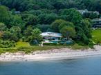 Set on over two acres of pristine waterfront along the shoreline of Sands Point, this custom-built contemporary beach house, masterfully designed by award-winning architect Daniel Schartzman, is a true architectural masterpiece. Thoughtfully designed to embrace its breathtaking setting on the Long Island Sound, the residence features soaring walls of glass and oversized windows that bathe the interiors in natural light while capturing uninterrupted water views from nearly every angle. A timeless work of art, the home showcases exceptional design elements including cedar-paneled ceilings, a bamboo front door, natural travertine-clad walls, grasscloth wallpaper, and a sculptural curved double-sided fireplace that anchors the open living spaces. At the heart of the home lies a stunning glass-enclosed conservatory - blurring the lines between indoors and nature - creating a tranquil centerpiece that sets this residence apart.This residence has 4/5 bedrooms, 3.5 custom bathrooms, and an attached garage. The main-level primary suite opens directly to a serene waterfront terrace through sliding glass doors. Each bathroom is exquisitely appointed with bespoke vanities, intricate tilework, and beautiful stained glass windows. Seamless floor-to-ceiling storage solutions throughout the home contribute to its clean, minimalist aesthetic.Outdoors, a sprawling sun-soaked patio provides the perfect setting for both relaxation and entertaining, leading to a private sandy beach and a sunken outdoor shower - an ideal touch for rinsing off after a day by the water. Additionally, a resort-style in-ground pool with a cascading waterfall feature enhances the outdoor experience, while a spacious pergola offers a shaded retreat to take in the sweeping coastal panorama. The home is framed by a round pebble driveway and lush, manicured landscaping, creating a picture-perfect setting. A gated entry courtyard provides a dramatic sense of arrival, unveiling a stunning walkway that leads through the conservatory and on to the front entrance. Meticulously maintained and masterfully designed, this waterfront haven represents the pinnacle of elevated coastal living.