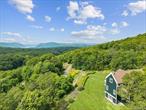Wooded retreat meets modern comfort in this breathtaking Garrison home, perched atop a gently rolling hill on 5.3 private, park-like acres and abutted by state land. With its blend of soaring ceilings, warm woodwork, and sweeping Hudson River views, this home strikes a rare balance: grand in scale, yet deeply cozyâ€”perfectly suited for both year-round living and weekend escapes. Double barn doors welcome you to a covered porch entry that greets you with soaring ceilings and custom hardwood floors. Past the entry, the main level flows effortlessly, centered around an expansive living room anchored by a dramatic floor-to-ceiling stone fireplace. A formal dining room and covered porch provide front-row seats to panoramic views of the Hudson Highlands, while the chefâ€™s kitchenâ€”equipped with top-tier Miele and Viking appliancesâ€”opens to the deck for effortless indoor-outdoor dining and entertaining. Nearby media room adds a quiet, intimate space for movie nights or unwinding with a book. Upstairs, french doors open to a private balcony, ideal for coffee with a view at sunrise or stargazing at night. The dreamy primary suite is a private sanctuary, boasting vaulted ceilings en suite spa bathroom with soaking tub and spacious vanity. Three additional bedrooms and two full baths mean flexible options for family, guests, or a flexible work-from-home setup. Walkout lower level includes a half bath and open rec space perfect for a home gym, playroom, or additional living area. Outdoors, enjoy a beautifully sited heated pool surrounded by natural landscaping and peaceful wooded views. Just steps away, a one-bedroom guesthouse above the detached garage offering privacy and comfort for visitors, extended family, or creative pursuits. Luxurious, private, and surrounded by nature, yet only minutes to Metro North, Cold Spring village and endless outdoor adventure, this home captures everything that makes the Hudson Valley so special.