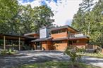 Perched sixty feet above the Muddy Kill Creek in Stone Ridge, this newly built home, named &rsquo;&rsquo;Fern Hollow&rsquo;&rsquo;, blends mid-century modern inspiration with one-of-a-kind details, offering both striking design and emotional warmth that sets it apart from standard new construction. The result is a modern treehouse, with dramatic views of the creek as it weaves through the lush wooded landscape. The builders took great care to infuse character into the home by incorporating reclaimed architectural pieces throughout. Vintage terrazzo floors, custom-designed door hardware, and an unforgettable walk-in closetâ€”crafted from the cabinetry of a 1960s libraryâ€”are just a few examples of the artistry. Every detail has been curated, creating a home that is elevated yet approachable. With a nod to Frank Lloyd Wright&rsquo;s sense of surprise, the foyer&rsquo;s understated character is bright and welcoming, giving way to the soaring main living space, where expansive glass walls frame the forest canopy and the creek below. A wood-burning fireplace provides warmth and a striking focal point, while two oversized doors extend the living area outward, opening directly to the decks and blurring the line between indoors and out. A hidden mechanized television drops down from above the fireplace, maintaining the clean lines of the room until it&rsquo;s time to gather for a movie night. The kitchen is equally thought out in form and function, with soapstone counters, custom oak cabinetry, a coffee/dry bar, wine fridge, and a dramatic picture window in place of a backsplash, looking directly into the forest. A disguised door is integrated into the kitchen cabinetry, leading to a hidden first-floor suiteâ€”perfect for guests, in-laws, or a quiet office retreat. The sleek, moody mudroom just off the carport (with an EV charging station) leads to a powder room and laundry area with a chute, as well as a generous flex space suited to a gym, media room, or playroom. Upstairs, spalted maple floors run throughout. The spa-like primary suite is a tranquil, spacious retreat that opens to a hot tub ready private deck where you can unwind with the creek&rsquo;s quiet rhythm as your backdrop. Completing the suite is a spa-like bathroom featuring a luxurious soaking tub and walk-in shower, along with a walk-in closet whose custom millwork nods to its origin as a mid-century library. Another guest room, a stylish full bathroom, and an open loft leading to a large deck round out the second floor, offering both comfort and flexibility for family or visitors. Additional features include polished concrete floors with radiant heat on the first level, mini-splits throughout for cooling and additional heating, and wiring in place for a whole-house generator. Set at the end of a private road, the property is secluded and peaceful, with frontage on both sides of the Muddy Kill Creek and mature trees that create a timeless natural sanctuary, yet it&rsquo;s just minutes to the center of Stone Ridge and a short drive to Accord, High Falls, New Paltz, and the area&rsquo;s farm stands, breweries, and dining destinations.